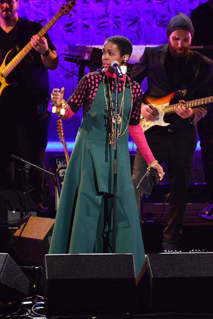 Lauryn Hill performing in green jumper in front of bass and guitar player