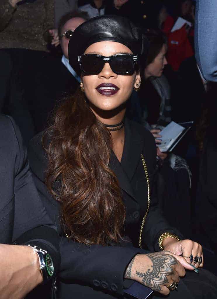 Rihanna in black leather hat and ponytail sitting with others at event