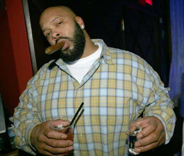 Suge Knight smoking cigar and holding alcoholic drink in right hand and a shotglass in left hand