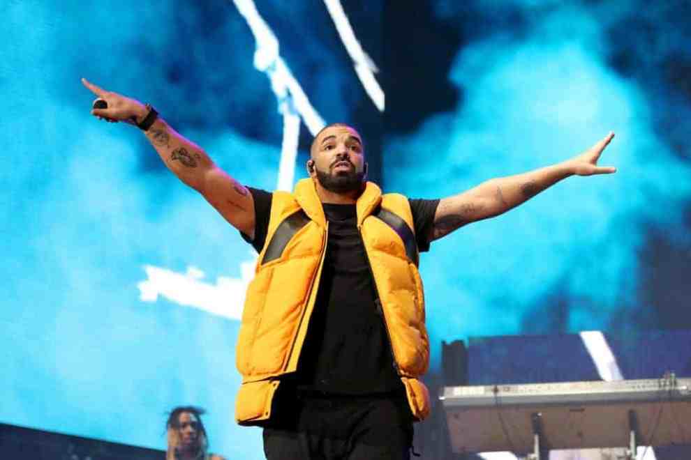 Drake performing in yellow puffy vest in front of blue smoky background
