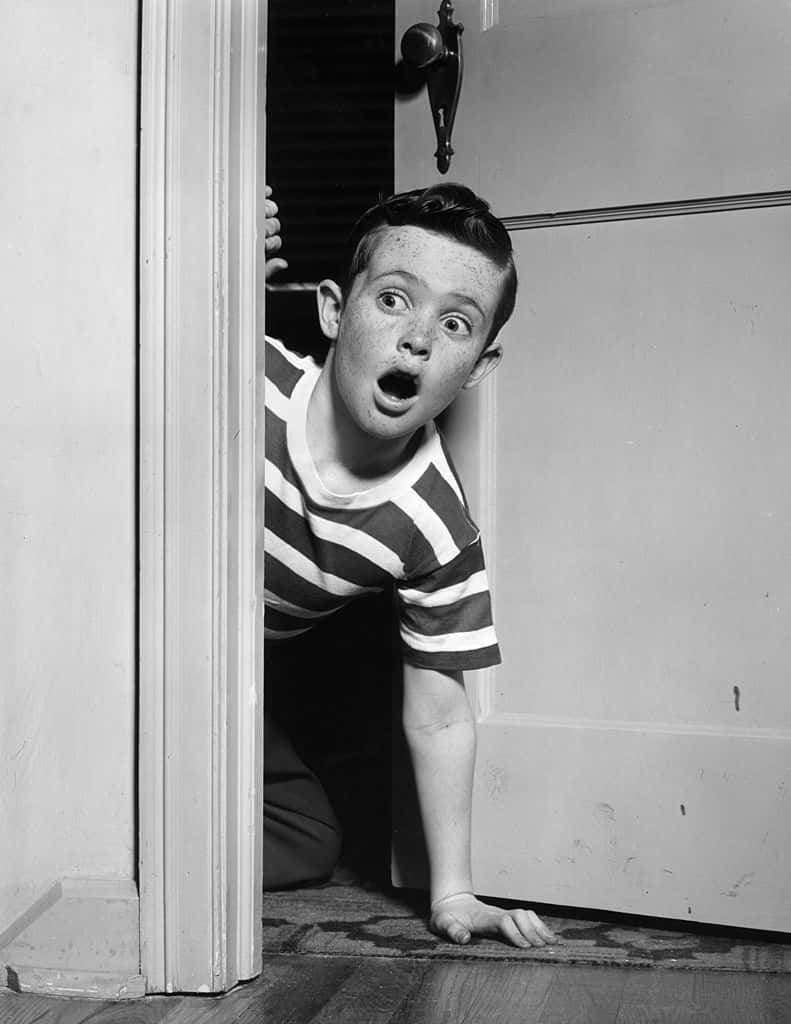 A young boy looks surprised as he kneels on the floor