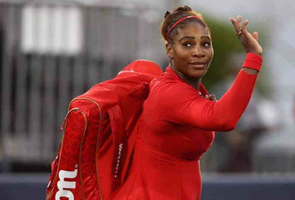Serena Williams in all red tennis gear waves as she exits the court