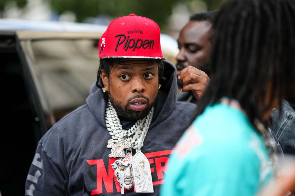 Westside Gunn wears a red with embroidered black and white print pattern cap, large silver and diamonds chain necklaces, a black t-shirt, a dark gray hoodie sweater, a large diamond earring, outside the Kidsuper show, during Paris Fashion Week - Menswear Spring/Summer 2023, on June 24, 2022 in Paris, France.